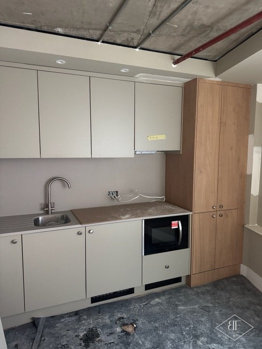 Kitchen units and tall oak-effect cupboard installed while floor protection is still down