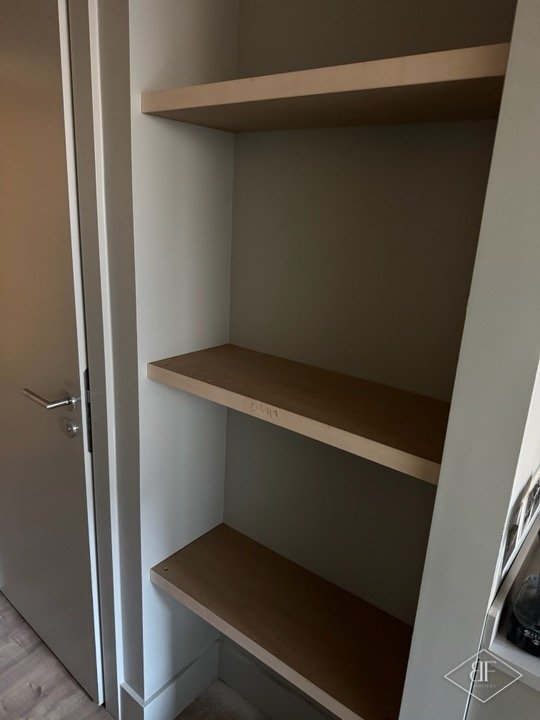 Built-in cupboard with oak-effect shelves beside a grey door