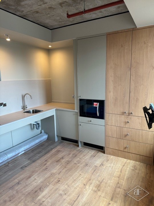 Finished kitchenette with tall oak-effect storage and low-level sink unit, flooring protected