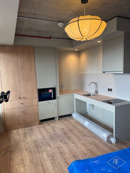 Fitted kitchen and tall storage wall with warm downlights and a lantern pendant