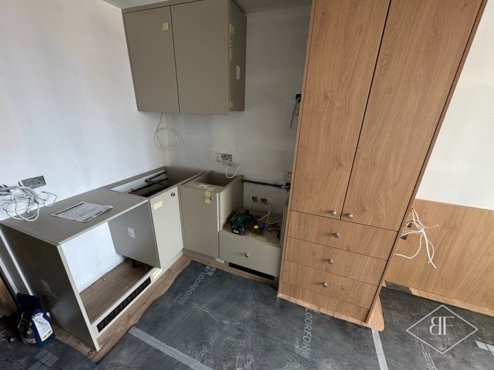 Tall oak-effect larder cupboard and grey base units mid-installation under floor protection
