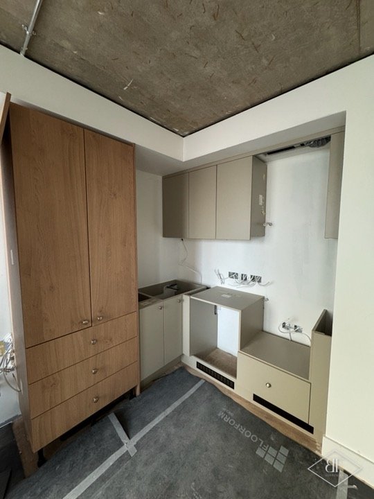 Tall wood-effect cupboards and base units being installed beneath an exposed concrete ceiling