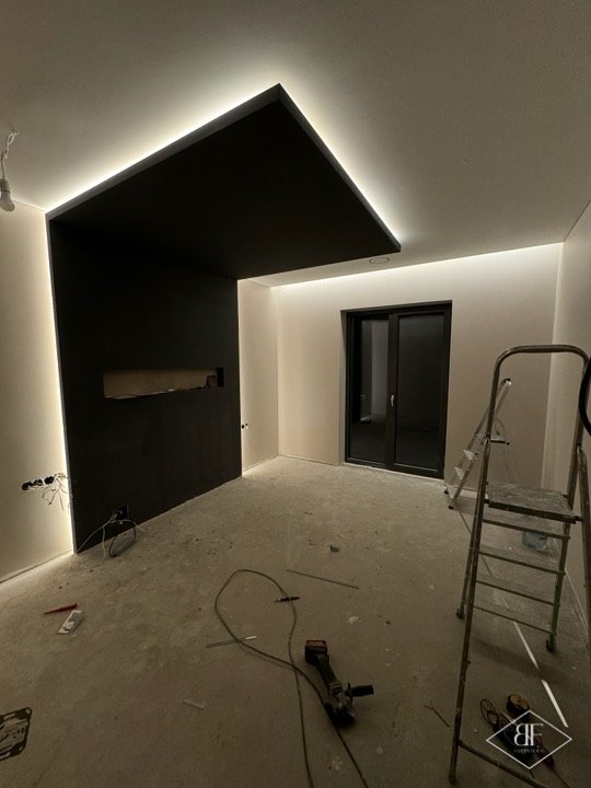 Dark ceiling drop with glowing LED cove edge above a feature wall, unfinished room