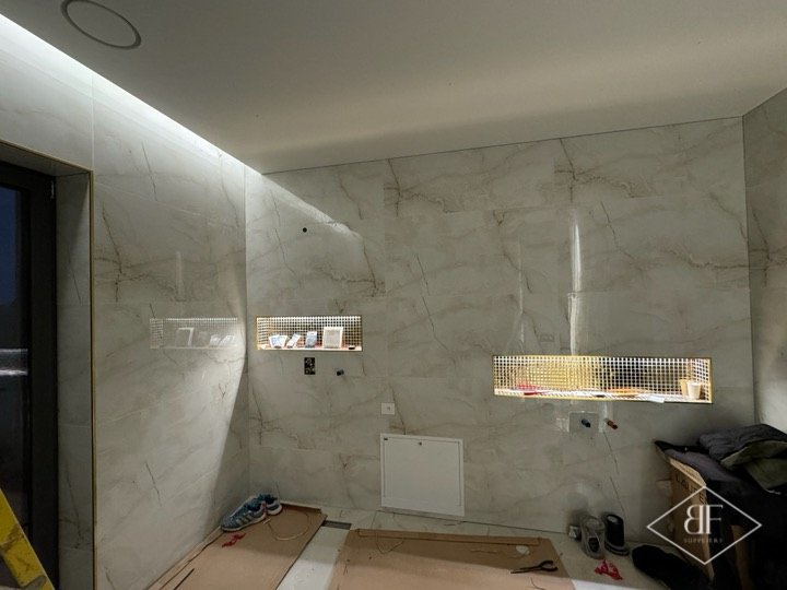 Marble-effect wall with illuminated recessed niches and ceiling cove lighting, still under construction