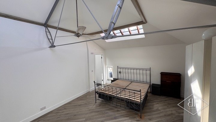 Vaulted loft bedroom with steel roof ties and rooflights, bed frame in place