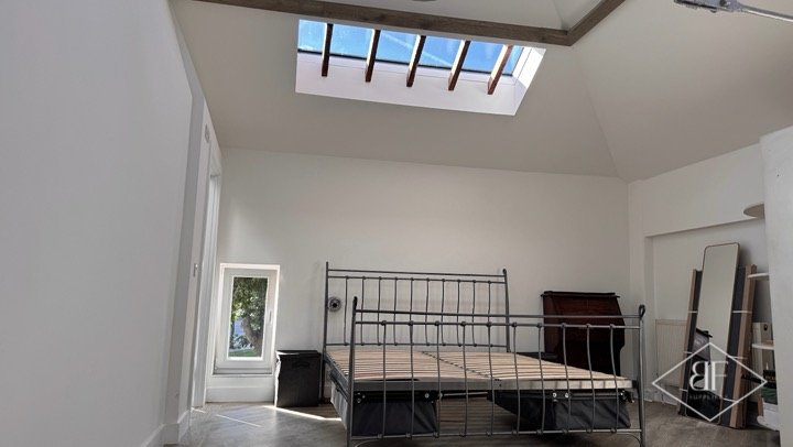 Finished loft bedroom with large rooflight, white walls and wood-effect flooring