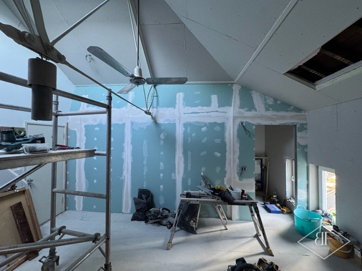 Plasterboarded loft interior with scaffold, tools and open ceiling hatch during renovation