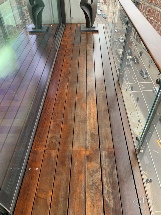 Long hardwood balcony deck running past glass panels, partly cleaned