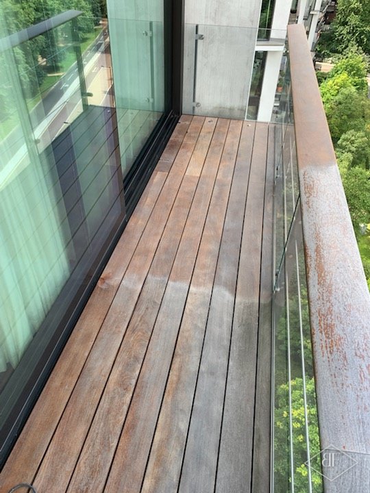 Hardwood balcony decking partly cleaned, showing the colour returning beside the glass balustrade