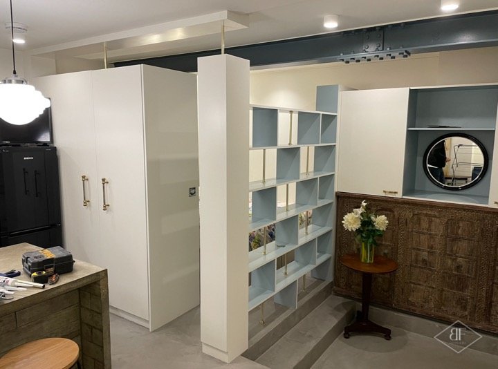 Tall white wardrobes beside a blue shelving divider, with a vintage cabinet to the right