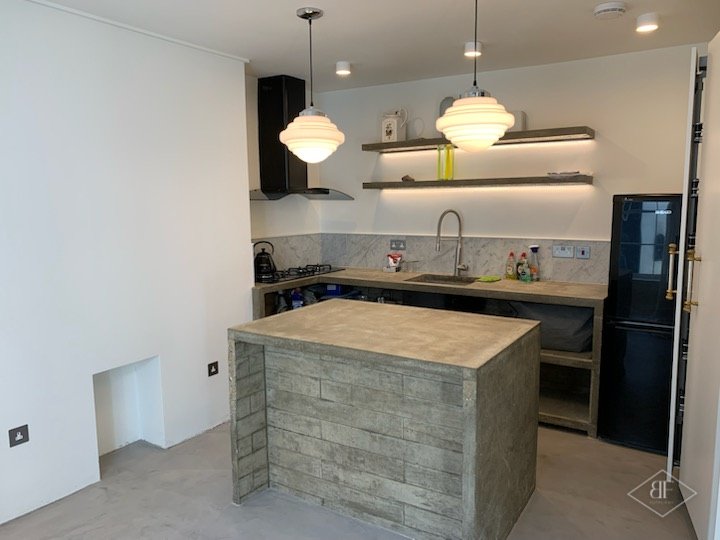 Kitchen island and worktop with concrete effect finish and a black fridge, in Kensington
