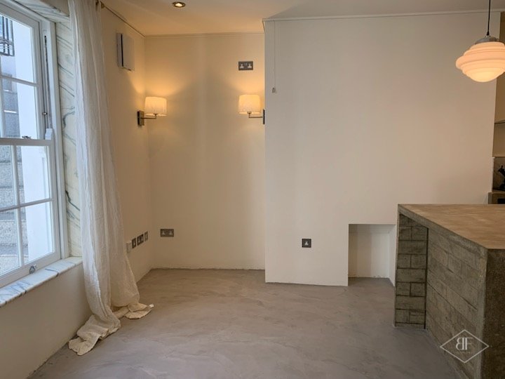 Studio living space with sash window, wall lights and a microcement floor