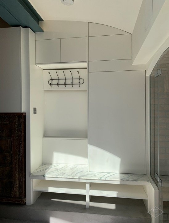 Hallway storage with coat hooks, built-in cupboards and a bench with marble effect top