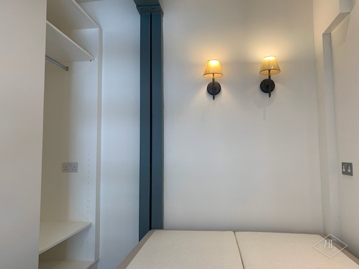 Fitted wardrobe space with shelves and a hanging rail beside two wall lights
