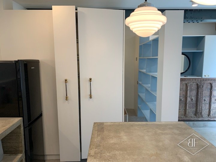 White wardrobe doors with brass handles beside the kitchen island and blue shelving
