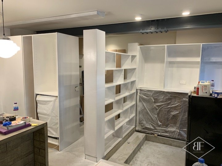 Shelving and wardrobe units being fitted, with protective sheeting and tools on the worktop