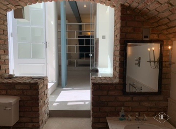 Bathroom with exposed brick arch, mirror and basin, looking toward the glazed door