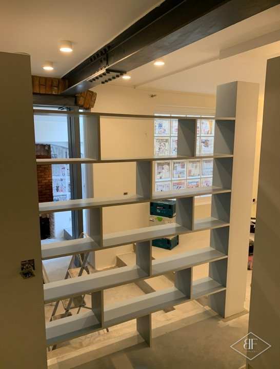 Looking through the open shelving divider toward the bright living area and steel beam