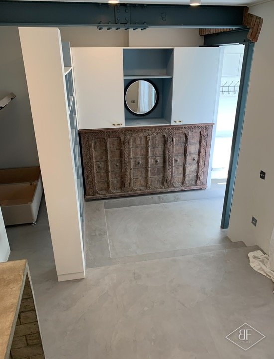 Cabinet with round mirror above a carved sideboard, with new microcement floor in the basement flat