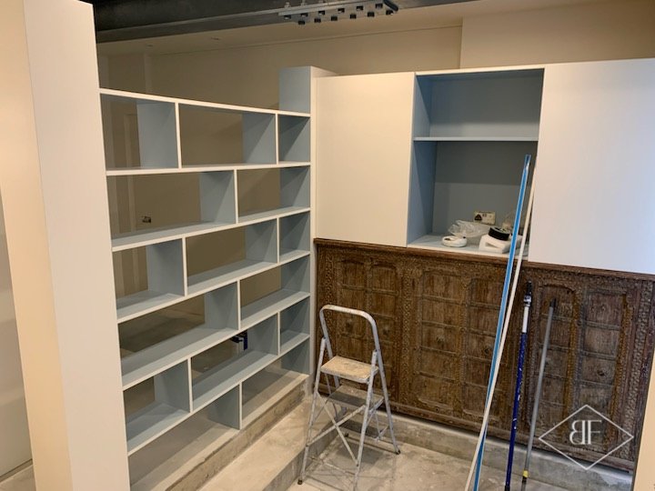 Open white cube shelving beside a tall blue-backed alcove during fit-out