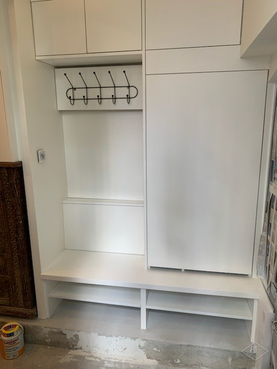 Built-in hallway bench with coat hooks and tall white cupboards in the basement flat