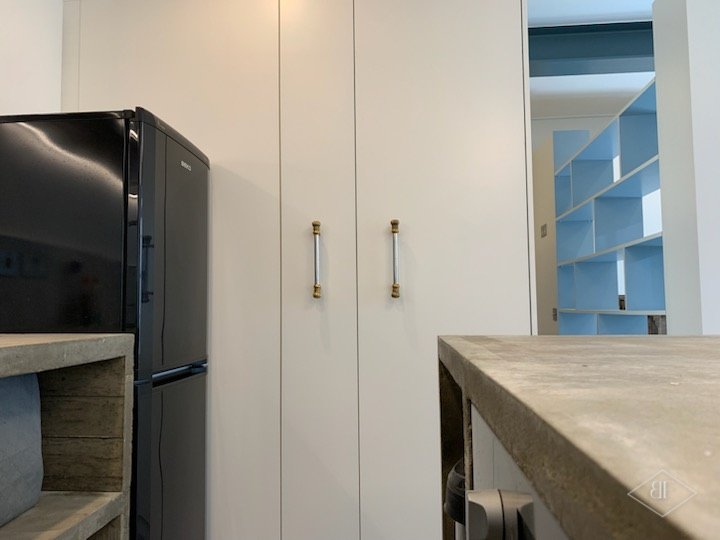 White fitted wardrobe doors with brass handles beside a concrete-topped kitchen island