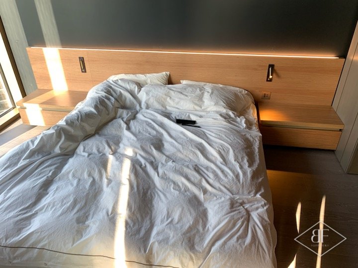 Bed with an oak headboard panel and integrated lighting, before bedding was made up