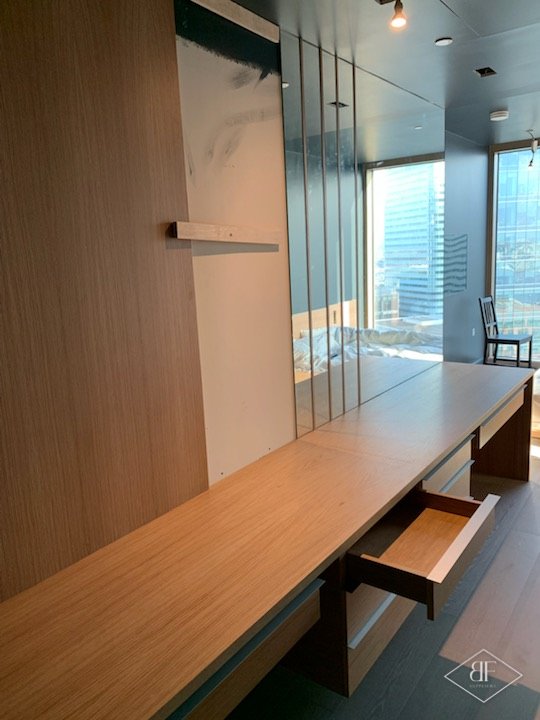 Oak desk unit with a drawer open and a tall mirror panel by a window