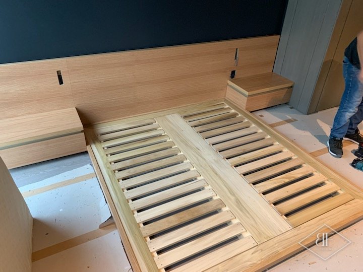 Oak slatted bed base fitted beside bedside units and headboard panel during installation
