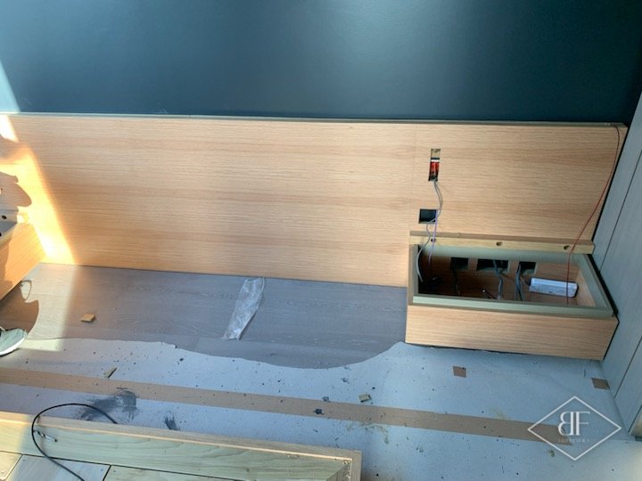Headboard panel and bedside cabinet being fitted in a bedroom with floor protection