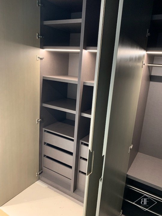Tall wardrobe with open shelving and pull-out drawers lit by integrated strip lighting
