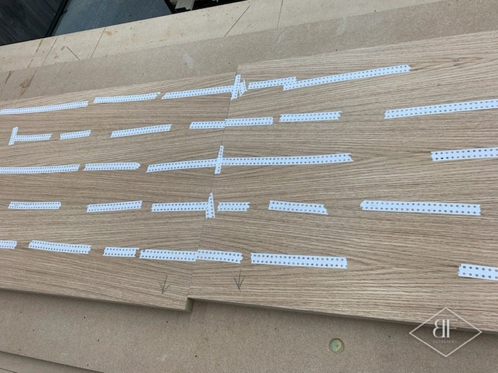 Oak veneer panel with edge banding strips laid out for preparation in the workshop