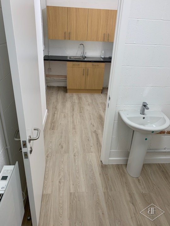 Kitchenette with oak-effect units and dark worktop beside a cloakroom basin
