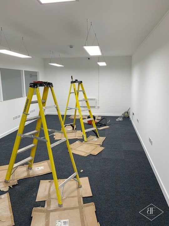 Finished office room with new blue carpet tiles and ceiling lights, floor protected