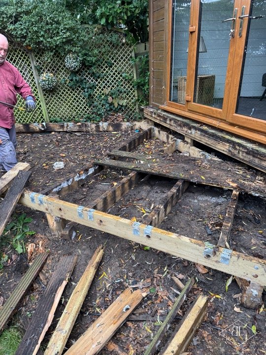 Old decking stripped back to the joists beside a garden cabin