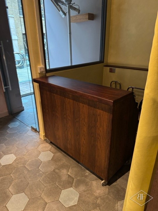 Wooden booth with polished top and panelled front near a glazed entrance