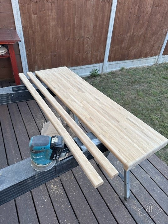 Solid wood top and strips being sanded outdoors on trestles before assembly
