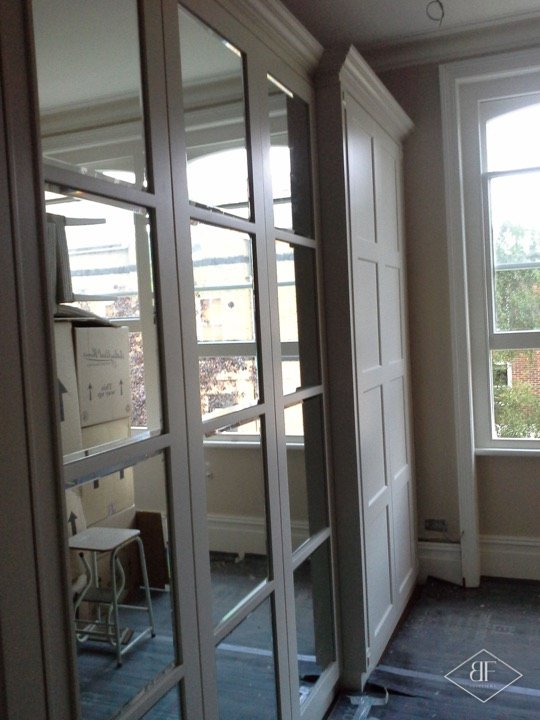Glazed mirror-panel wardrobe doors beside a tall sash window during installation