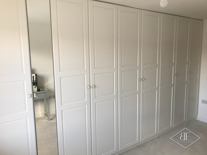 Run of white panelled wardrobe doors with knobs along a bedroom wall in London