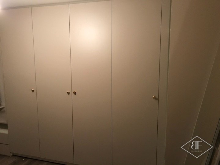 Plain painted wardrobe doors with small knobs fitted along a bedroom wall
