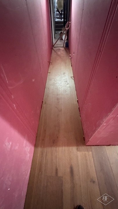 Long engineered oak floor running down a narrow corridor between boarded walls