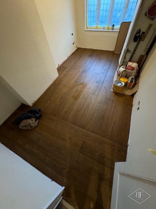 Newly laid dark oak plank flooring in a bright room with a tall window
