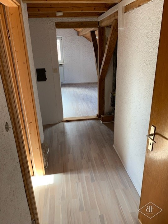 Light laminate flooring finished along a corridor beneath exposed timber beams in a Chelsea home