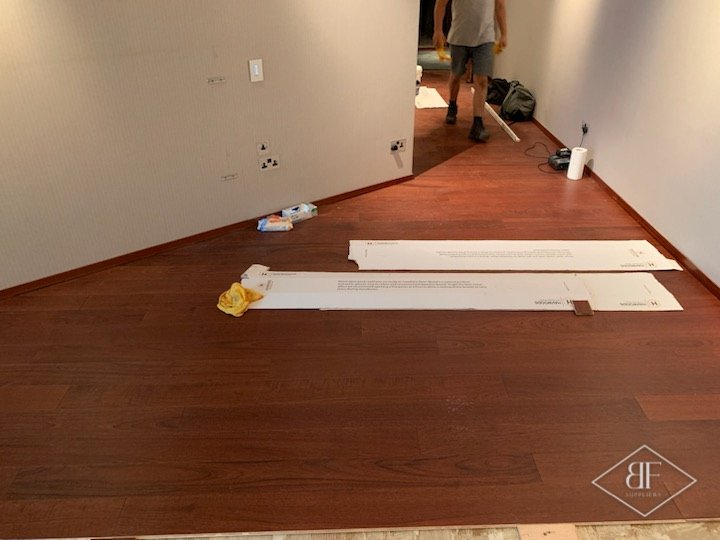 Red-brown hardwood boards being laid across a long room, with offcuts on the floor