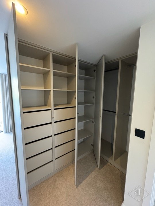Open wardrobe interior with shelves, drawers and hanging space behind handleless doors
