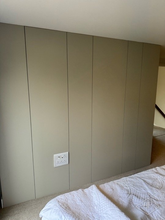 Full wall of flush handleless wardrobe doors beside a bed