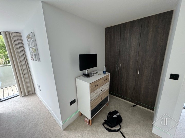 Dark wood-effect fitted wardrobe doors in a bright bedroom with balcony doors