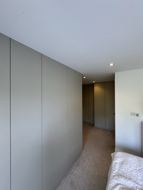 Long run of plain handleless wardrobe doors along a bedroom wall, finished