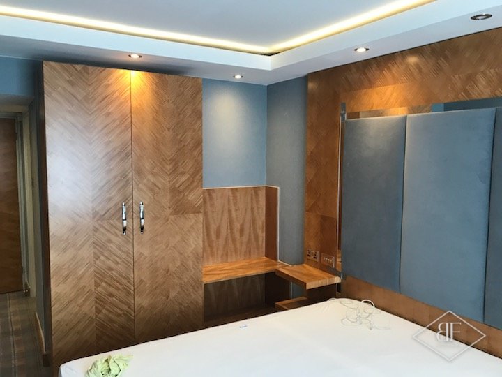 Tall chevron veneer wardrobe beside the upholstered headboard wall and bedside shelf