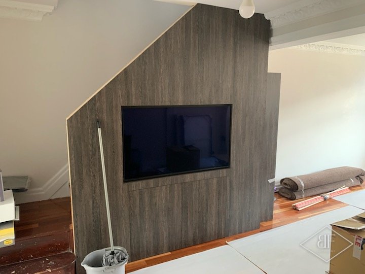 Angled wood-effect partition wall with mounted television in a house, during refurbishment